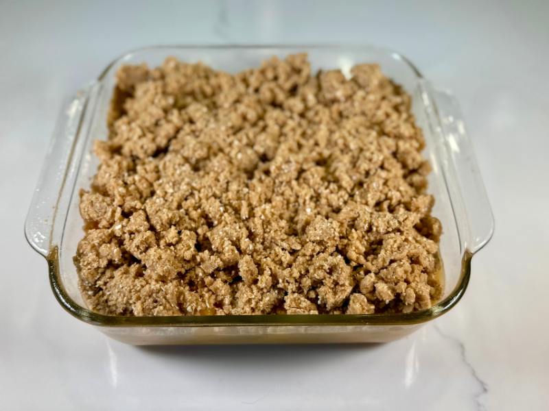 peach crisp with fresh peaches in a square glass baking dish.